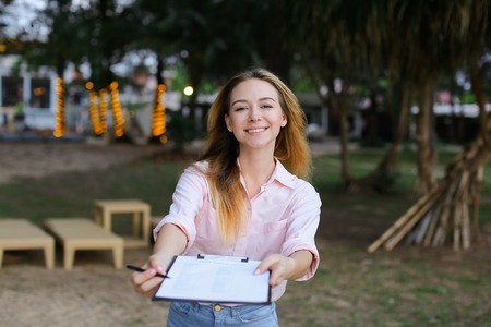Young businesswoman giving pen and documents outdoors, resort background. Concept of business and tourism.の写真素材