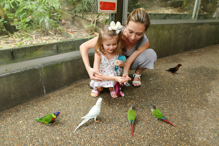 Young mother and little daughter enjoying with parrots outside. Concept of exotic animals, summer vacations in Thailand and tourism.の写真素材