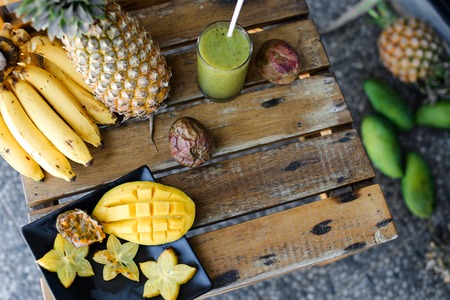 Carambola with mango in plate near bananas and pine-apple on wooden table. Concept of exotic fruits and tropical healthy food.