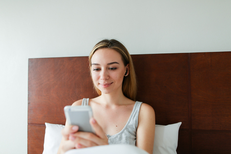 Young happy woman using wireless headphones and listening to music by smartphone. Concept of modern technology and resting on weekends in morning.の写真素材
