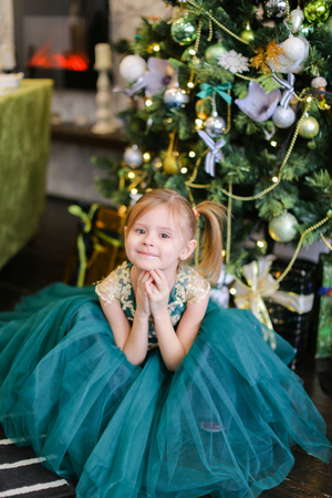Little cute girl wearing blue dress standing near Christmas tree. Concept of celebrating New Year, fashion and childhood.の写真素材