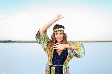 Caucasian woman with raised hand wearing black swimsuit and green beach robe standing on sand. Concept of summer clothes collection and fashion.の写真素材