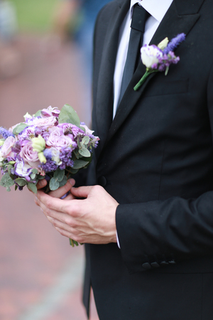 Caucasian groom wearing black suit and tie keeping bouquet of flowers. Concept of wedding.の写真素材
