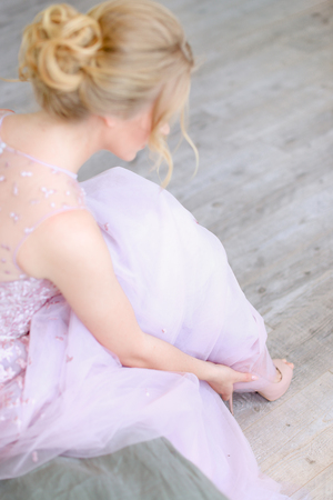 Back view of blonde bride touching shoe. Concept of bridal hairstyle and photo session.の写真素材