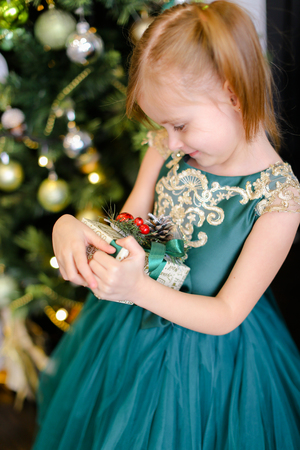 Little pretty girl with gift wearing dress and standing near Christmas tree. Concept of presents, childhood and winter holidays.の写真素材