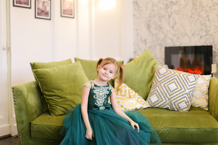 Little girl wearing dress and sitting on sofa. Concept of celebrating birthday and winter holidays.の写真素材