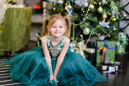 Little beautiful girl wearing blue dress standing near Christmas tree. Concept of celebrating New Year, fashion and childhood.の写真素材