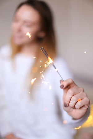 Blurred photo of american happy woman sitting with closeup bengal light near twinkling yellow garlands. Concept of handmade decorations for Christmas and New Year holidays.の写真素材
