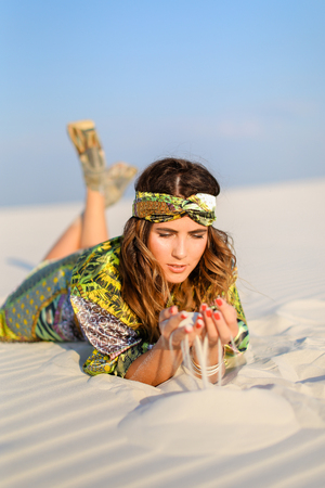 Young photo model wearing green beach robe lying on white sand. Concept of sunbathe and photo session in desert.の写真素材