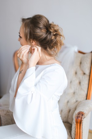 Caucasian bride dressing earrings. Concept of wedding preparing in morning.の写真素材