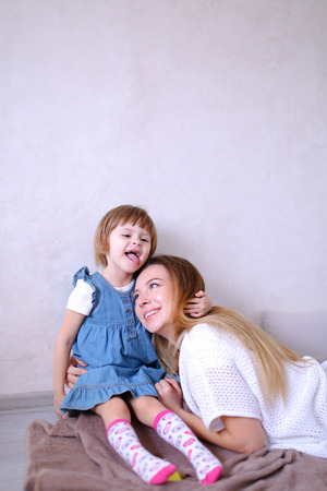Young mother hugging little daughter and sitting on bed. Concept of children, motherhood and leisure.の写真素材