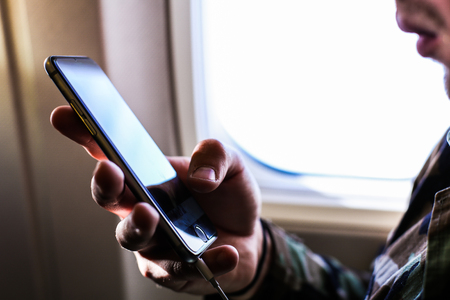 Closeup man using smartphone near window in airplane. Concept of modern technologe and low cost...