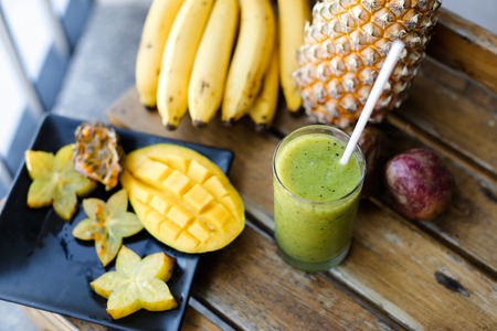 Tasty pine apple with bananas, carambola and mango standing on wooden chair, kiwi fresh juice. Concept of healthy food and exotic diet.の写真素材