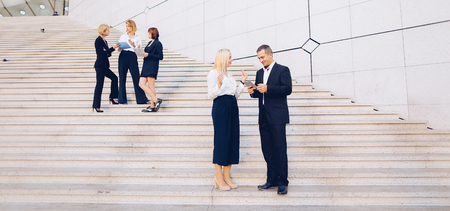Financial team members going down stairs with tablet, document case and talking by smartphone in  . Concept business partners leaving conference with positive emotions. Successful young people wear suits and shirts.の写真素材