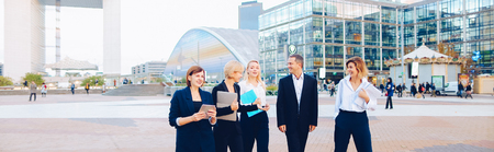 Members of business organization talking outside and smiling with document case and tablet in hands. Concept of walking biz team and resting outside. Group people dressed in suits and white shirts with close up faces.の写真素材