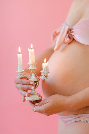 Closeup happy pregnant woman in underwear holding belly and keeping candles in pink monophonic background. Concept of expactant photo session.の写真素材