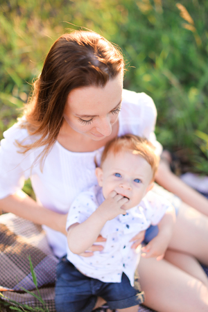 Young tender woman kissing little baby on plaid, grass on background. Concept of picnic, motherhood and nature.の写真素材