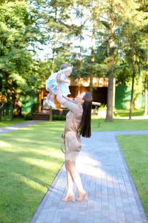 Young brunette mother wearing dress holding little baby in garden. Concept of motherhood and resting on open air in park.の写真素材