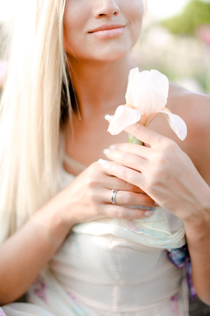 Blonde girl keeping irise flower and smiling. Concept of human beauty and flora, spring inspiration.の写真素材