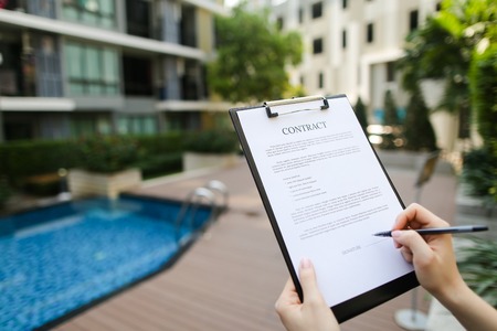 large hand portrait of subscribers sign contract on background of new building with swimming pool. concept of long-term rental housing or short-term apartment rental travel. Front used with Open Font Licenseの写真素材