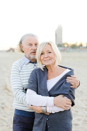 Senior husband hugging blonde caucasian wife in sand beach background. Concept of elderly couple and relationship.の写真素材