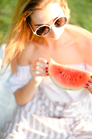 Young blonde caucasian girl in sunglasses eating watermelon. Concept of healty food and summer season, vegeterian lifestyle.の写真素材
