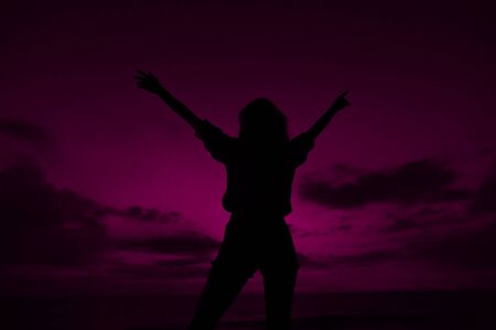 Female silhouette with raised hands on violet sunset sky background in Thailand. Concept of summer vacations, freedom and cheap last minute tours to southern countries.の写真素材