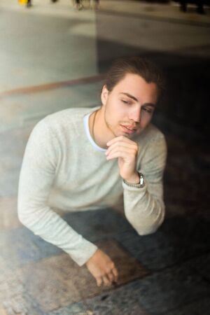 Young man wearing grey sweater sitting, reflection in window. Concept of tourist and resting.の写真素材