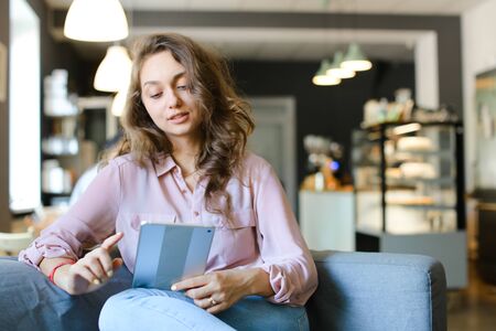 Young woman enjoying with fast internet by tablet and sitting at cafe. Concept of free hotspot at catering establishment and spending time with modern technology.の写真素材