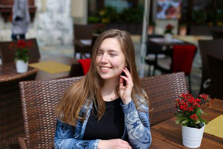 Young european girl sitting at cafe near red room flowers, wearing blue sweater. Concept of resting and waiting for lunch.の写真素材
