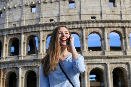 Young female tourist talking by smartphone in Colosseum background in Rome. Concept of advantageous tariff plan and last minute tours to Italy.の写真素材