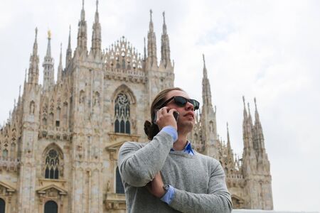 Caucasian tourist speaking by smartphone near Milan Cathedral, Italy. Concept of modern technology, advantageous tariff plan and landmarks.の写真素材
