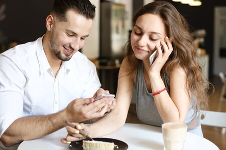 Young pretty girl talking by smartphone and sitting with man using hotspot at cafe. Concept of happy couple and relationship, modern technology and internet.の写真素材