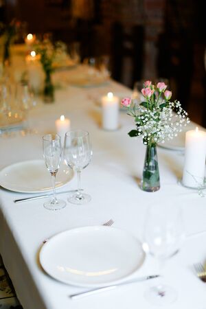 Bouguet of flowers, plates with forks and white candles on table. oncept of romantic dinner and catering establishment.の写真素材