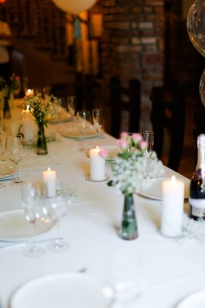Bouguet of flowers, white plates with forks and candles on table. oncept of romantic dinner and catering establishment.の写真素材