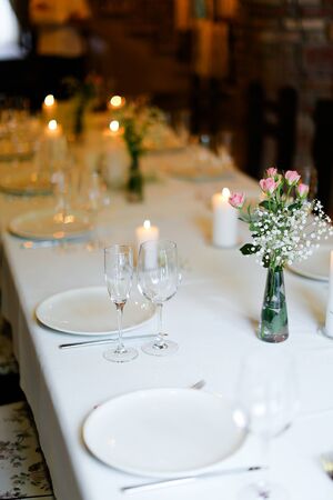 Bouguet of flowers, plates with forks and white candles on table. oncept of romantic dinner and catering establishment.の写真素材