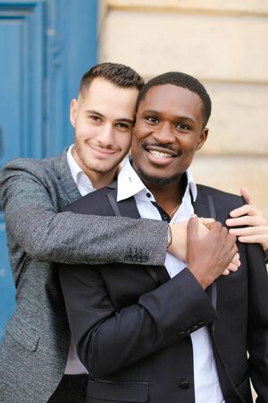 Portrait of two hugging boys, caucasian and afro american, wearing suits. Concept of gays and lgbt.の写真素材