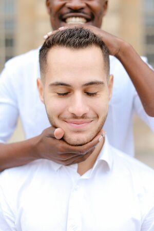 Portrait of caucasian man, afro american guy holding boy head by hands.の写真素材