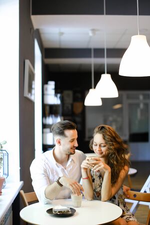 Young european husband hugging wife and sitting at cafe, drinking coffee. Concept of enjoing togetherness and having lunch.の写真素材