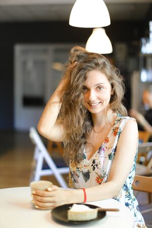 Young caucasian girl sitting with cake and cup of coffee at cafe. Concept of having lunch and resting at break.の写真素材