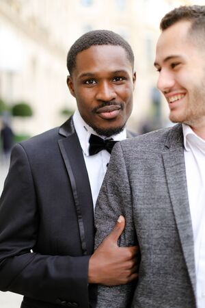 Focus on fro american handsome man hugging european boy wearing suit. Concept of gays and same sex couple.の写真素材
