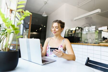 Young girl holding debit card near laptop. Concept of purchasing goods online and shopping by internet.の写真素材
