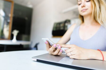 Focus on white smartphone and laptop, woman surfing internet. Concept of modern technology and purchasing online.の写真素材