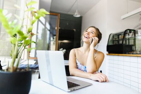 Pretty woman speaking by smartphone and using laptop at cafe. Concept of booking tour online.の写真素材