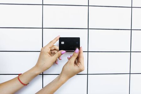 Hands holding debit card in white tile wall background. Concept of bank account and credit.の写真素材
