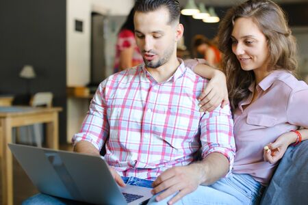Young woman and man using laptop at cafe and surfing. Concept of free hotspot and fast internet, modern technology and happy couple.の写真素材