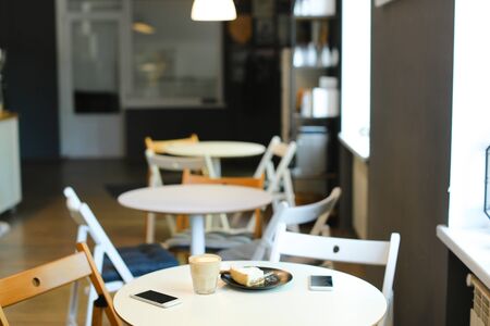 Empty cozy cafe with cups of coffe, smartphones and cake on table. Concept of interior and catering establishment, modern technology.の写真素材