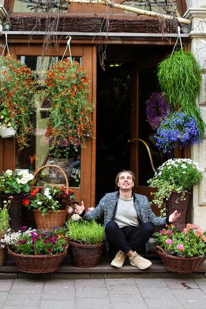Young male person sitting at flower shop near bouquets in baskets. Concept of business adn floristic art.の写真素材