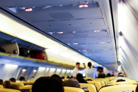Blurred photo of airplane interior and passengers with bags on shelves. Concept of cheap tickets and low cost flights.の写真素材
