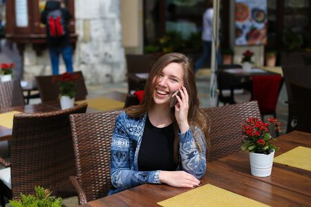 Young smiling female person speaking by smartphone at cafe near red flowers. Concept of modern technology and advantagous tariff plan.の写真素材